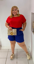 Load image into Gallery viewer, Woman in a red top and blue shorts standing in a boutique interior.