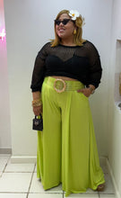 Load image into Gallery viewer, Woman wearing a black top and bright green pants with a flower in her hair, standing in a store.
